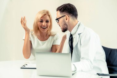 Erkek doktor hastane ofiste bayan hasta masada dizüstü bilgisayarda hastalar sağlık verilere bakarken konuştuğu. Sağlık ve tıbbi hizmet.