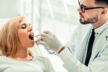 Genç yakışıklı dişçi diş diş kliniği, dişçi sandalyeye mutlu kadın hasta oturan incelenmesi. Diş Hekimliği bakım kavramı.