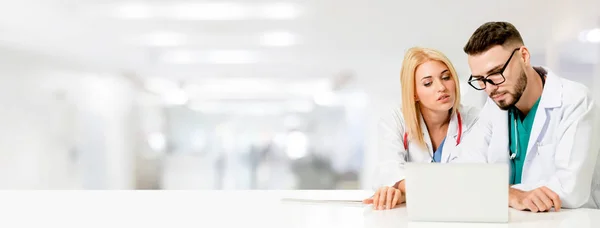 Doctor working with laptop computer at the office while having discussion with another doctor in the hospital. Medical healthcare and doctor service.