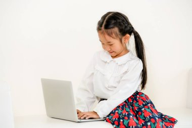 Beyaz koltukta oturan dizüstü bilgisayar kullanan küçük mutlu bir çocukluk. Çocukluk yaşam tarzı.