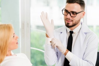 Genç yakışıklı dişçi mutlu kadın hasta diş hekimi diş kliniği sandalyede oturan ile konuşuyor. Diş Hekimliği bakım kavramı.