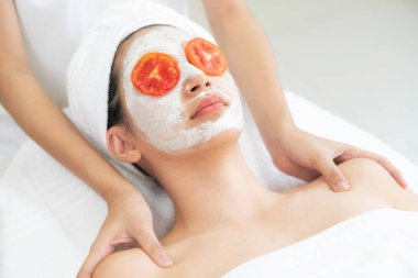 Beautiful woman having a facial mask treatment with tomato cream extract showing benefit of nature treatment. Anti-aging cosmetology, facial skin care and luxury lifestyle concept. clipart