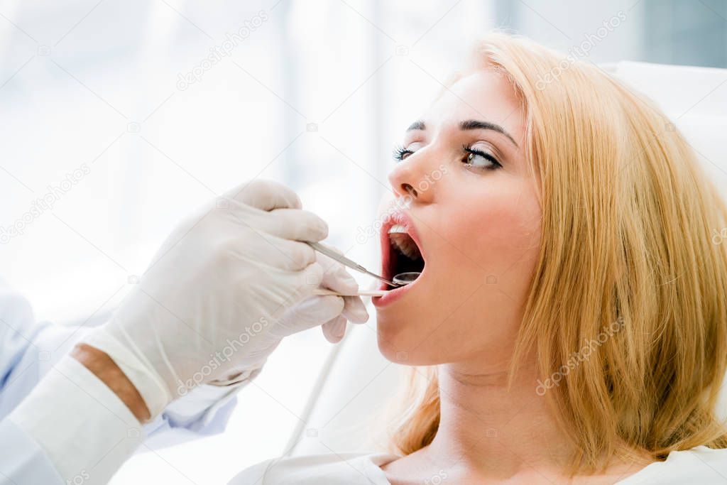 Young handsome dentist examining teeth of happy woman patient sitting on dentist chair in dental clinic. Dentistry care concept.