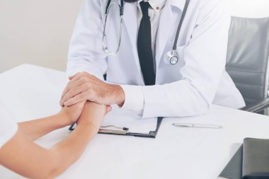 Erkek doktor hastane ofiste bayan hasta hasta ellerini tutarak yatıştırır. Sağlık ve tıbbi hizmet.