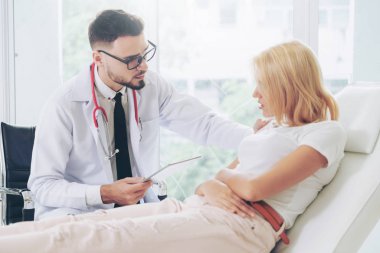 Erkek doktor konuşuyor ve Bayan hasta hastane ofisinde inceleyerek. Sağlık ve tıbbi hizmet.