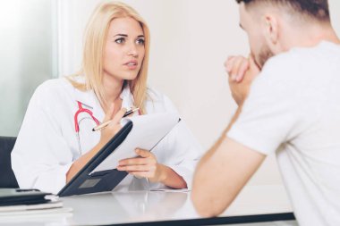 Kadın doktor konuşuyor ve erkek hasta hastane ofisinde inceleyerek. Sağlık ve tıbbi hizmet.