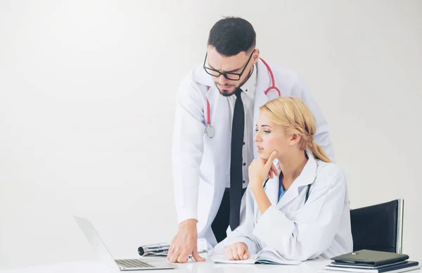 Doctor at hospital office working on laptop computer on the table with another doctor having discussion about patients health.