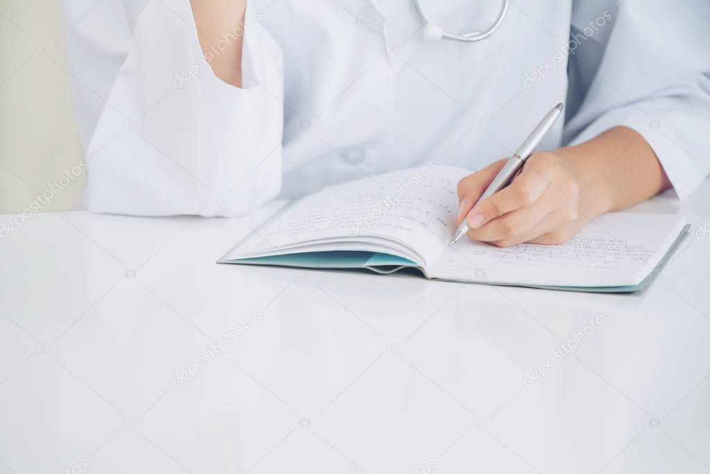 Close up shot of doctor writing on notebook report at the office in hospital. Healthcare professional.