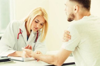 Kadın doktor konuşuyor ve erkek hasta hastane ofisinde inceleyerek. Sağlık ve tıbbi hizmet.