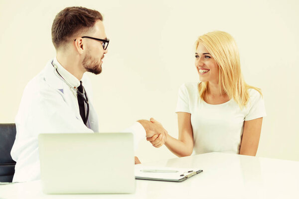 Мужчина-врач пожимает руку пациентке в больничном кабинете. Здравоохранение и медицинское обслуживание
.