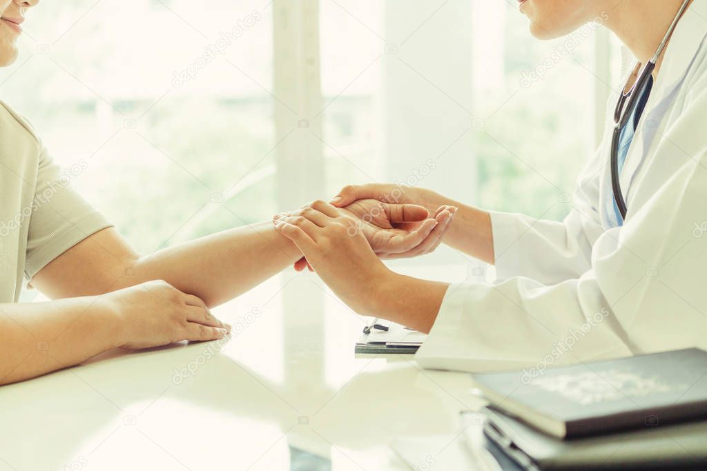 Woman doctor talks to female patient in hospital office while examining the patients pulse by hands. Healthcare and medical service.