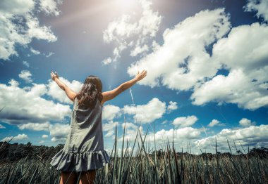 Genç güzel kadın kolları mavi güneşli gökyüzüne yaz gününde yayılan yeşil çim çayır üzerinde. Kaçış ve meditasyon kavramı.