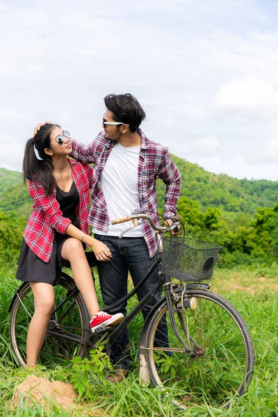 幸福的年轻夫妇的男人和女人骑自行车在草地上的山上 爱和旅游生活方式的概念 — 图库照片