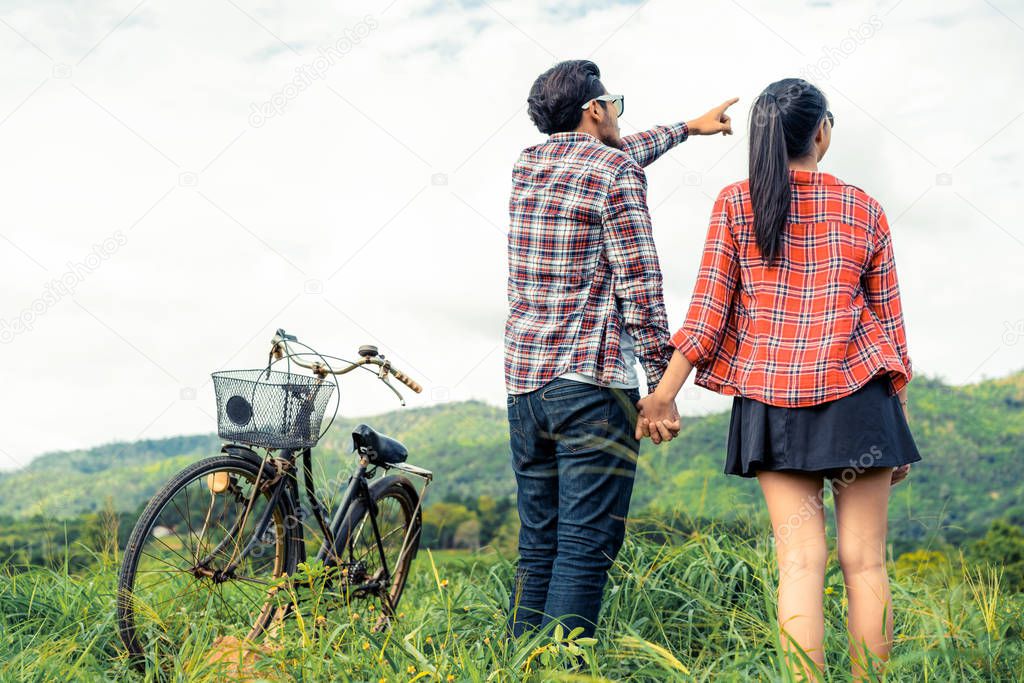 Happy young couple of man and woman ride bicycle at green grass field on the hills. Love and travel lifestyle concept.