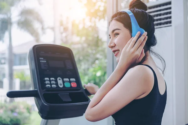 Young woman runner listens to music and runs on treadmill in fitness gym class. Healthy lifestyle concept.