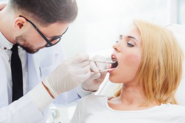 Genç yakışıklı dişçi diş diş kliniği, dişçi sandalyeye mutlu kadın hasta oturan incelenmesi. Diş Hekimliği bakım kavramı.