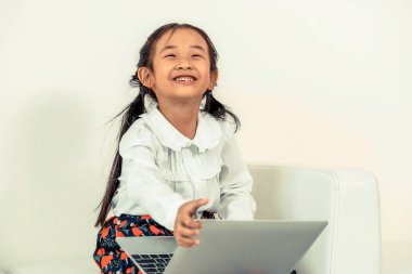 Beyaz koltukta oturan dizüstü bilgisayar kullanan küçük mutlu bir çocukluk. Çocukluk yaşam tarzı.