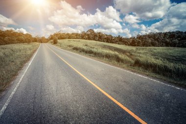 Tepe yaz günü mavi gökyüzünde üzerinde beyaz bulutlar altında yeşil çim sahası üzerinden karayolu yol. Yol yolculuk seyahat konsepti.