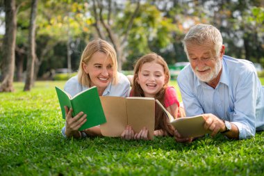 Mutlu aile birlikte ve yalancı kamu parki yeşil çim kitap okumak. Küçük kız çocuk anne ve babayla açık havada bahçe içinde öğrenme. Eğitim ve aile yaşam tarzı.