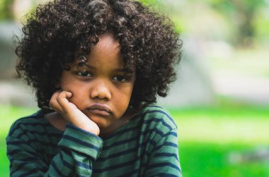 Mutsuz küçük Afro-Amerikan çocuk parkta oturan sıkılmış. Boy gösteren negatif duygu. Çocuk sorun kavramı.