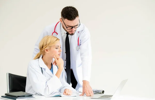 Doctor at hospital office working on laptop computer on the table with another doctor having discussion about patients health.