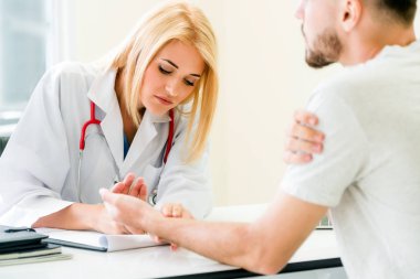 Kadın doktor konuşuyor ve erkek hasta hastane ofisinde inceleyerek. Sağlık ve tıbbi hizmet.
