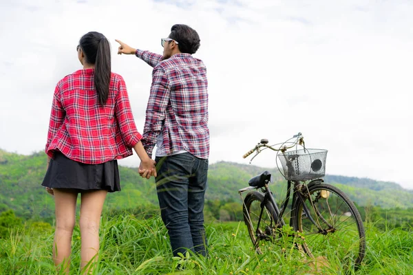 男と女の幸せな若いカップルの丘に緑の芝生のフィールドで自転車に乗る 愛と旅行のライフ スタイル コンセプト — ストック写真