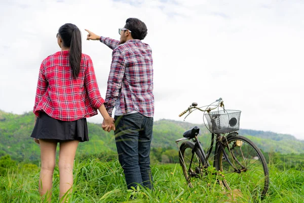 幸福的年轻夫妇的男人和女人骑自行车在草地上的山上 爱和旅游生活方式的概念 — 图库照片