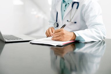 Masada oturan ve hastane office belge raporda yazılı erkek doktor. Tıbbi sağlık personeli ve doktor hizmeti.