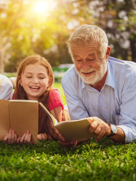 Happy family read books together and lying on green grass in public park. Little girl kid learning with father in outdoors garden. Education and family lifestyle.