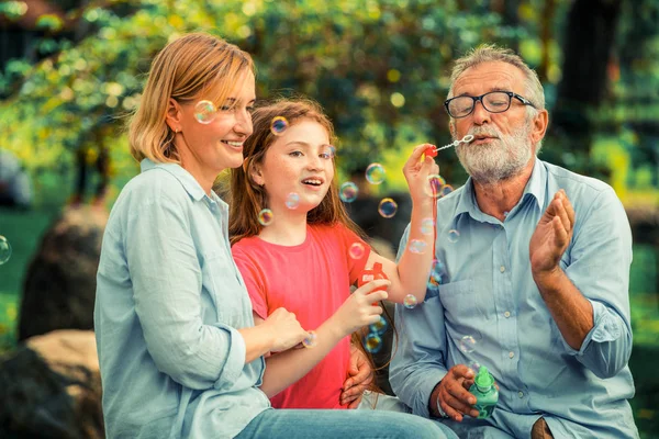 Happy family blows soap bubbles together while going vacation on weekend in the garden park in summer. Kid education and family activities concept.