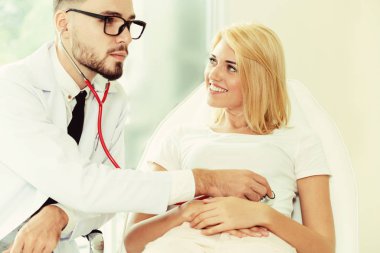 Erkek doktor konuşuyor ve Bayan hasta hastane ofisinde inceleyerek. Sağlık ve tıbbi hizmet.