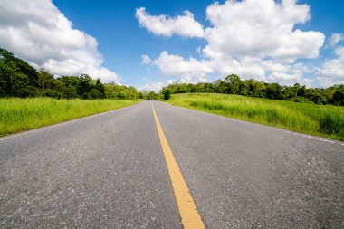 Tepe yaz günü mavi gökyüzünde üzerinde beyaz bulutlar altında yeşil çim sahası üzerinden karayolu yol. Yol yolculuk seyahat konsepti.