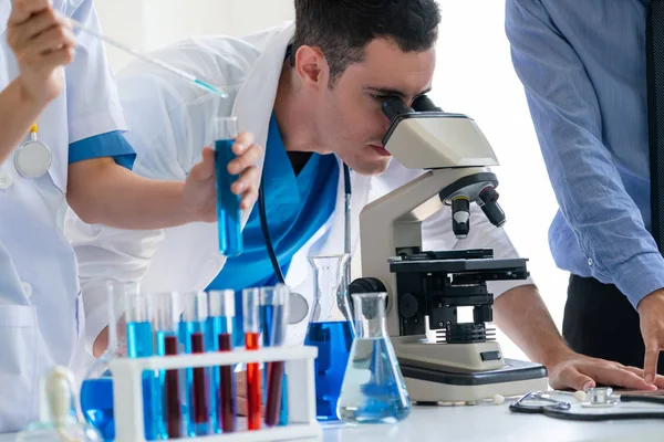 Group of scientists wearing lab coat working in laboratory while examining biochemistry sample in test tube and scientific instruments. Science technology research and development study concept.