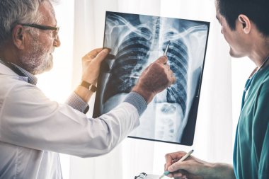 Üst düzey erkek doktor röntgen filmi ile başka bir Doktor hastanede çalışırken hastanın göğüs yaralanmaları bakarak. Tıbbi sağlık personeli ve doktor hizmeti.