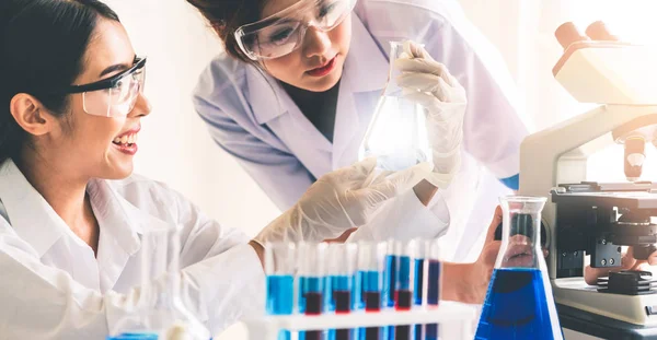 학자들은 시험관 장비로 생화학 표본을 조사하면서 실험실에서 작업하는 실험실 코트를 — 스톡 사진