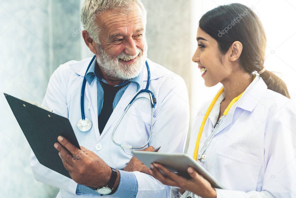 Senior male doctor using tablet computer while discussing with another doctor at the hospital. Medical healthcare staff and doctor service.