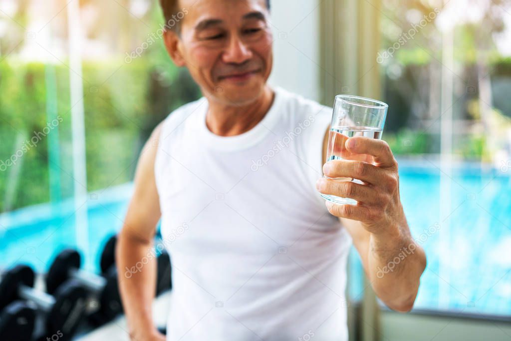 Senior man drink mineral water in gym fitness center after exercise. Elderly healthy lifestyle.