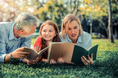 Mutlu aile birlikte ve yalancı kamu parki yeşil çim kitap okumak. Küçük kız çocuk anne ve babayla açık havada bahçe içinde öğrenme. Eğitim ve aile yaşam tarzı.