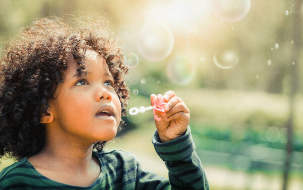 Счастливый маленький ребенок пускает мыльный пузырь в школьном саду. Концепция детских развлечений
.