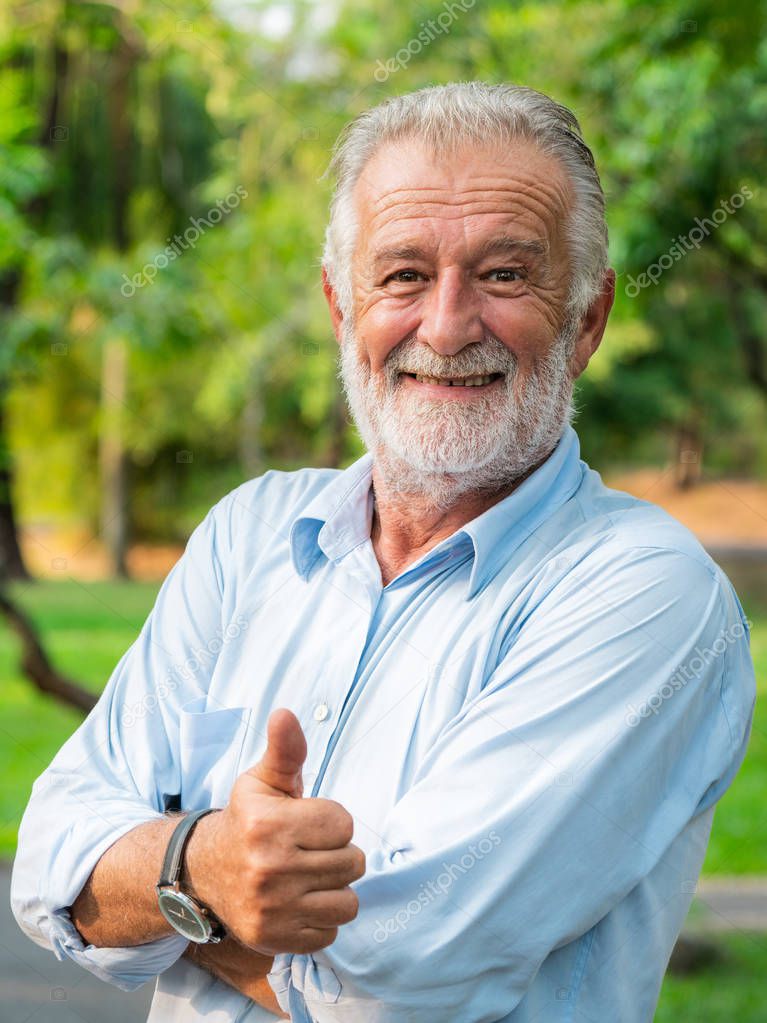 Portrait of happy senior man standing in the park. Elder health and retirement concept.