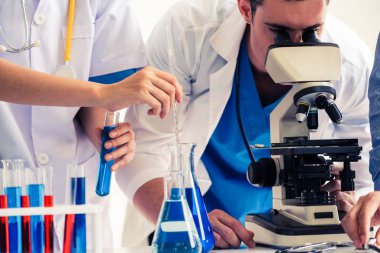 Laboratuvarda deney tüpü ve bilimsel aletlerdeki biyokimya örneklerini incelerken laboratuvar önlüğü giyen bir grup bilim adamı. Bilim teknolojisi araştırma ve geliştirme konsepti.