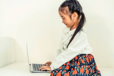 Beyaz koltukta oturan dizüstü bilgisayar kullanan küçük mutlu bir çocukluk. Çocukluk yaşam tarzı.