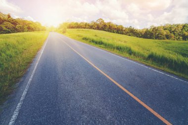 Tepe yaz günü mavi gökyüzünde üzerinde beyaz bulutlar altında yeşil çim sahası üzerinden karayolu yol. Yol yolculuk seyahat konsepti.