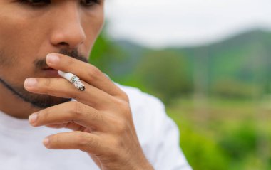 Genç adam açık havada ve doğa arka planda Sigara İçilmeyen. Sigara, seçici odak.