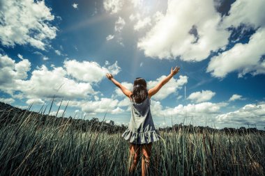 Genç güzel kadın kolları mavi güneşli gökyüzüne yaz gününde yayılan yeşil çim çayır üzerinde. Kaçış ve meditasyon kavramı.