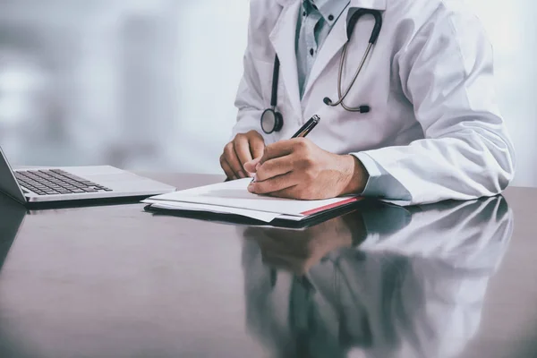 Männlicher Arzt Der Tisch Sitzt Und Krankenhausbüro Einen Dokumentarbericht Schreibt — Stockfoto