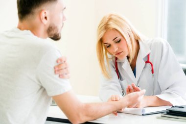Kadın doktor konuşuyor ve erkek hasta hastane ofisinde inceleyerek. Sağlık ve tıbbi hizmet.