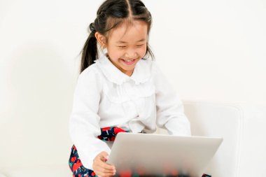 Beyaz koltukta oturan dizüstü bilgisayar kullanan küçük mutlu bir çocukluk. Çocukluk yaşam tarzı.