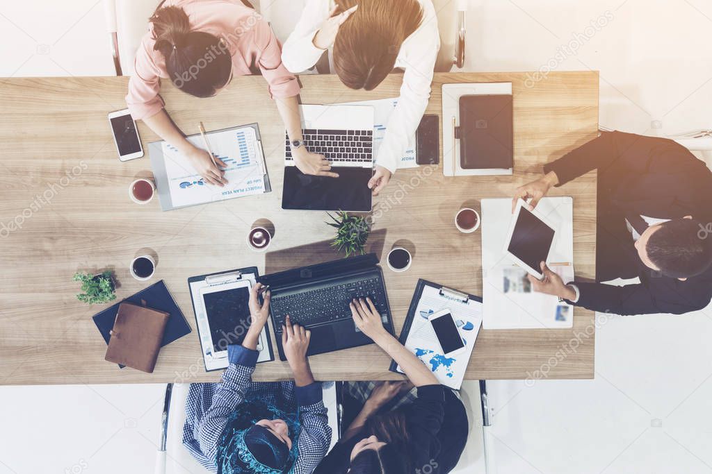 Top view of businessman executive in group meeting with other businessmen and businesswomen in modern office with laptop computer, coffee and document on table. People corporate business team concept.